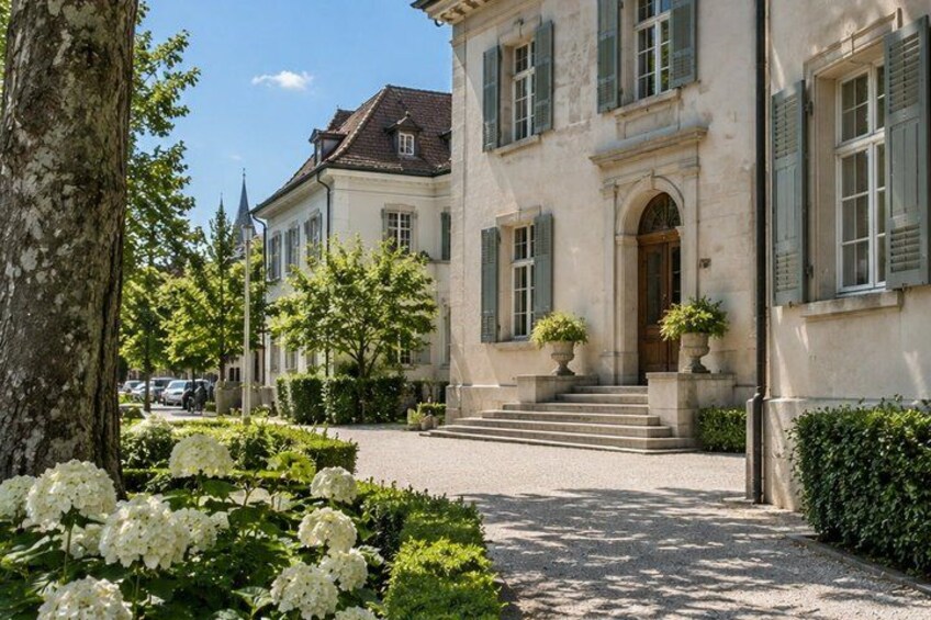 A classical building with a symmetrical facade, a central entrance, and a well-maintained garden with white flowers. 5