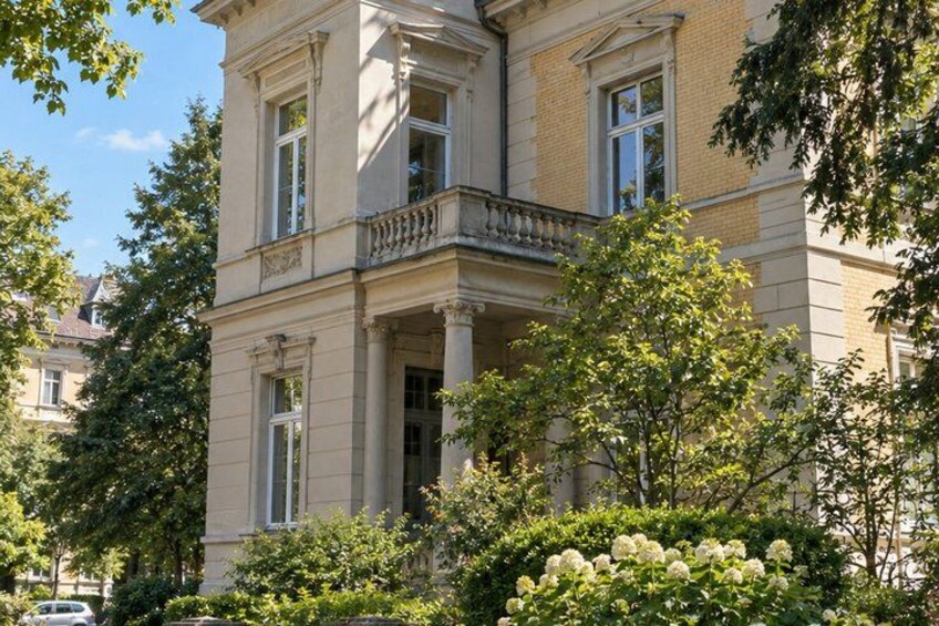 A classical building with a balcony, surrounded by lush greenery and trees. 4