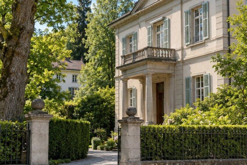 A classical building with a balcony, surrounded by a well-maintained hedge and a tree. 3