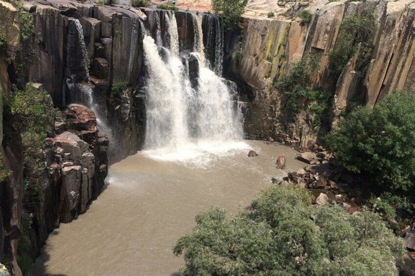 A waterfall cascading into a pool surrounded by rocky cliffs and greenery. 4