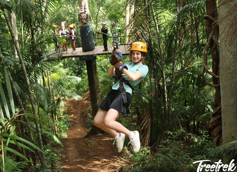 Une personne qui fait de la tyrolienne à travers une forêt dense, équipée d’un harnais de sécurité et d’un casque. 1