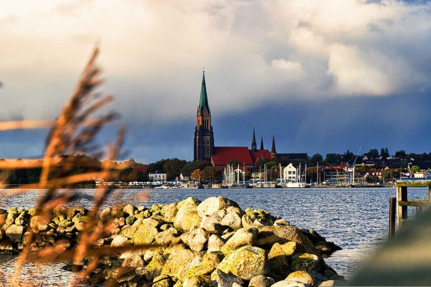 A river with a rocky shore, a church with a tall spire, and a town in the background. 3