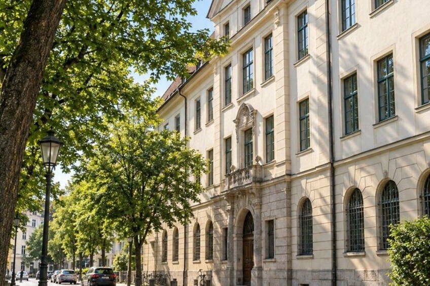 A classical building with arched windows and a balcony, surrounded by trees and parked cars. 3