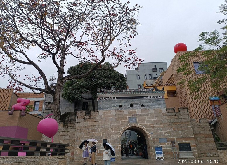 Una puerta tradicional china con un árbol en primer plano y un edificio moderno al fondo. 5