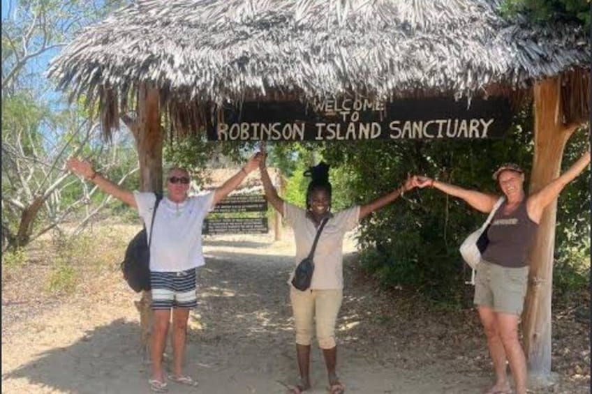 Three people standing in front of a sign that reads 'Welcome to Robinson Island Sanctuary.' 1