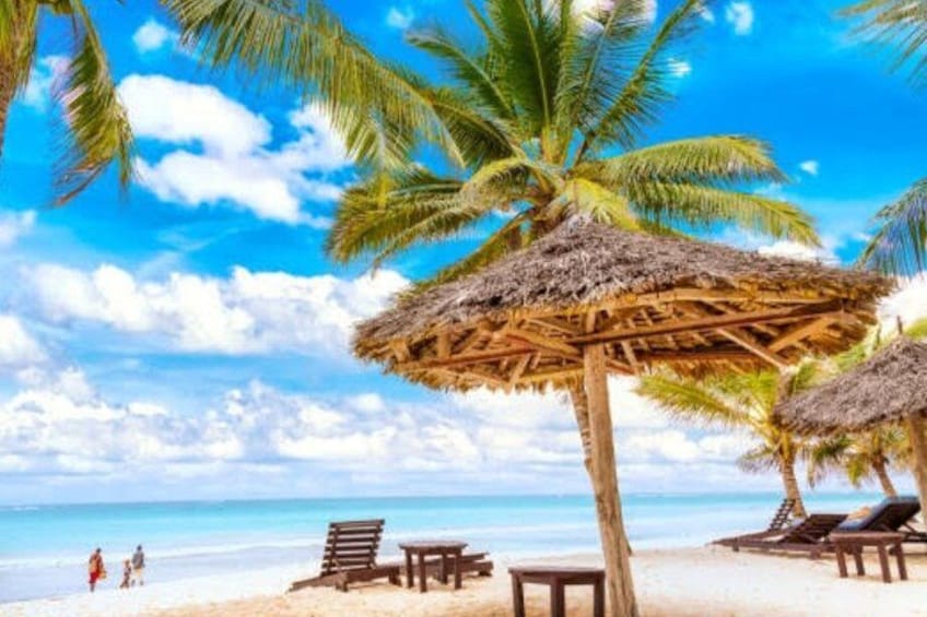 A beach with palm trees, a thatched umbrella, and lounge chairs. 3