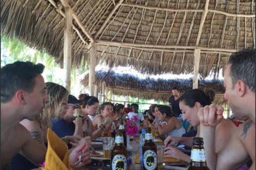 A group of people sitting at a table with drinks, under a thatched roof structure. 4