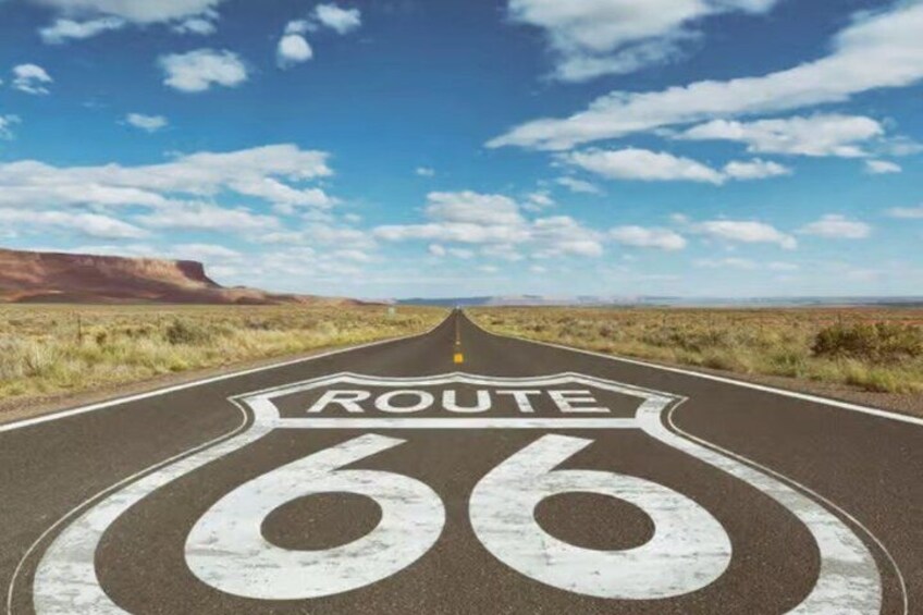 A road with Route 66 markings, surrounded by a flat landscape and a clear blue sky. 2