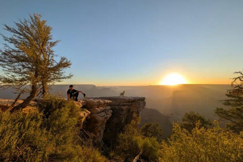 A person standing on a rock ledge overlooking a canyon with a sunset in the background. 3