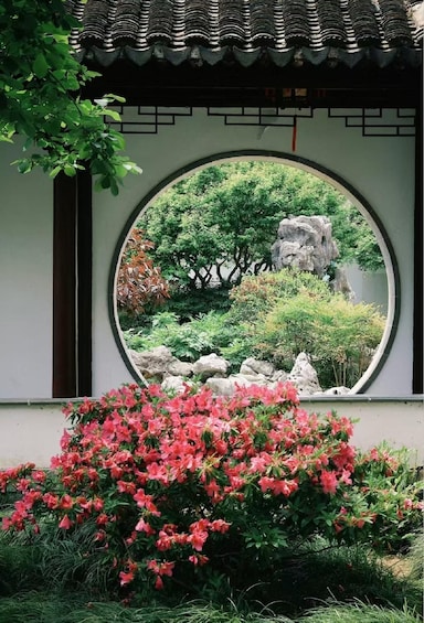 Un edificio japonés tradicional con una ventana circular, exuberante follaje y azaleas rosadas. 2