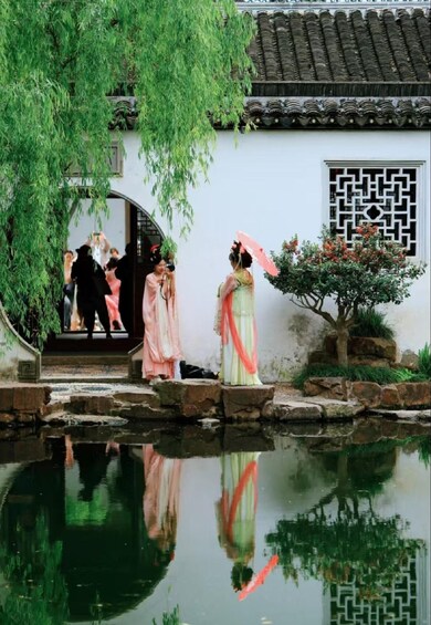 Un jardín chino tradicional con un puente de piedra, un estanque que refleja el paisaje y un edificio con tejado de azulejos y ventanas decorativas. 3