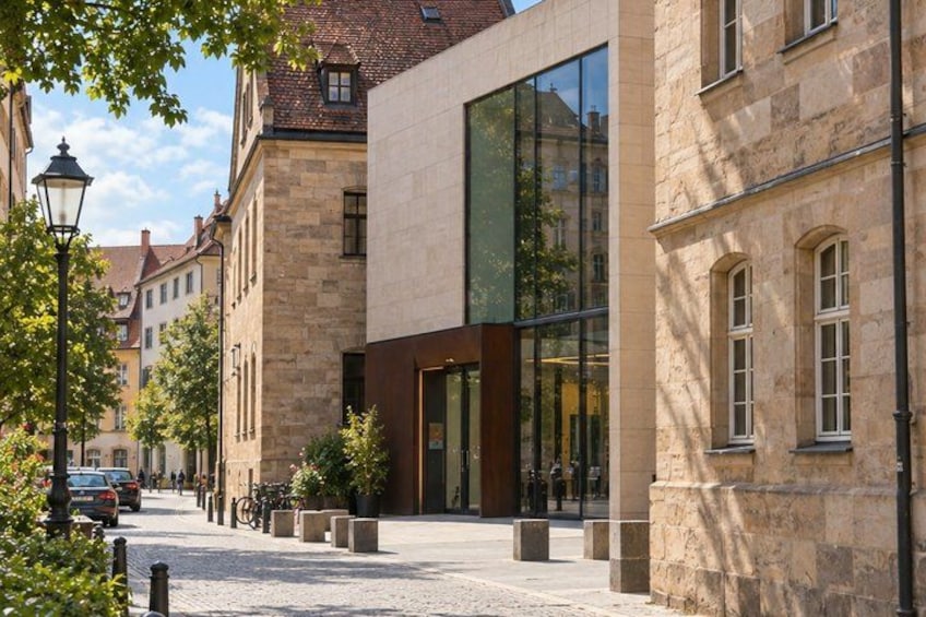 A cobblestone street lined with historic buildings, a modern glass building, and a lamppost. 5