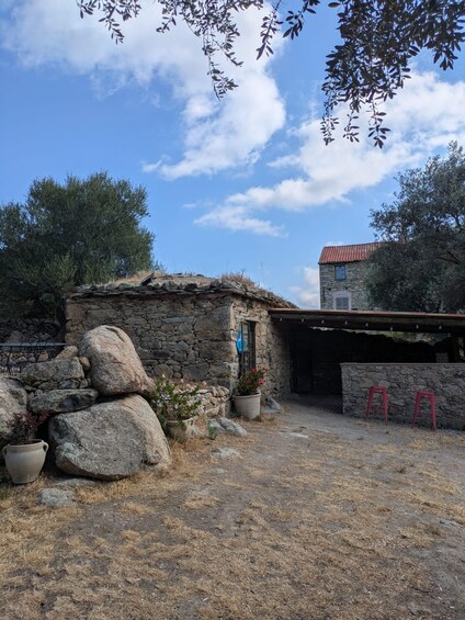 A rustic stone building with a red-tiled roof, a stone wall entrance, and a small garden with potted plants. 4