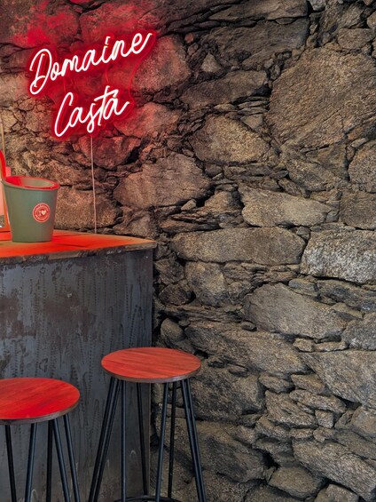 A stone wall with a neon sign reading 'Domaine Costa' and a green bucket with a red interior. 2