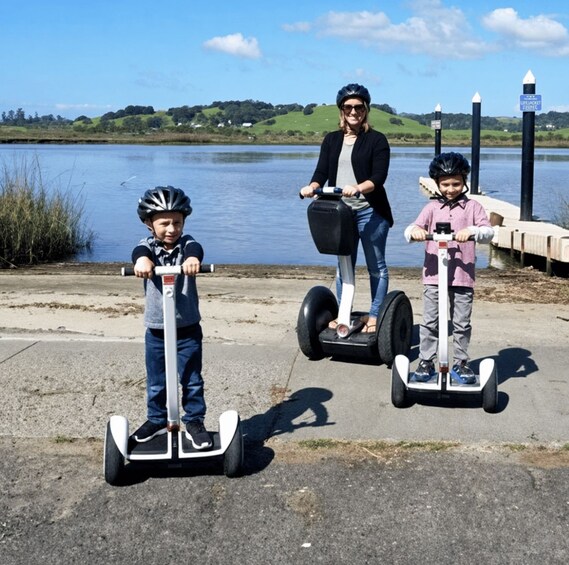 Three people on segways near a lake with a dock and a signpost in the background. 4