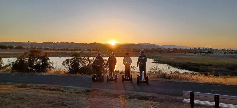 A sunset over a body of water with four people on segways. 1