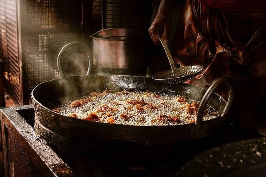 Une personne cuisine dans une grande poêle ronde et noire, et de la vapeur s’en échappe, ce qui indique que les aliments sont chauds. 2