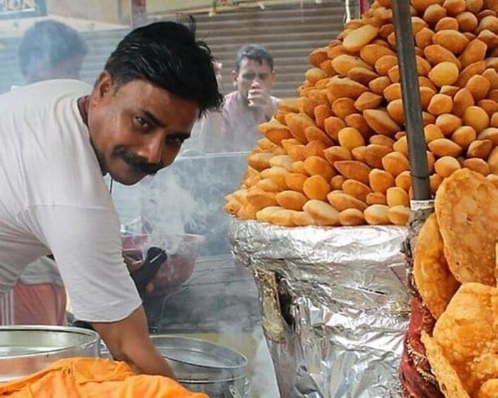 Un vendeur de nourriture de rue prépare des plats, avec une pile de beignets et une marmite sur le feu, le tout visible. 3