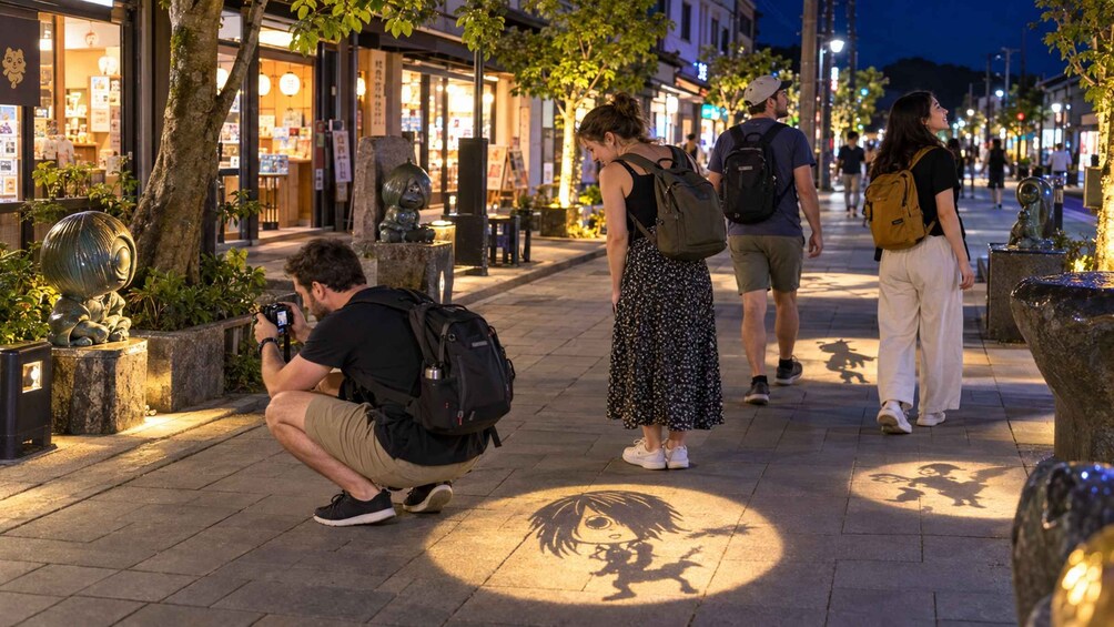 Una persona agachada tomando una foto, una mujer caminando y un hombre con una mochila en una calle urbana de noche. 3
