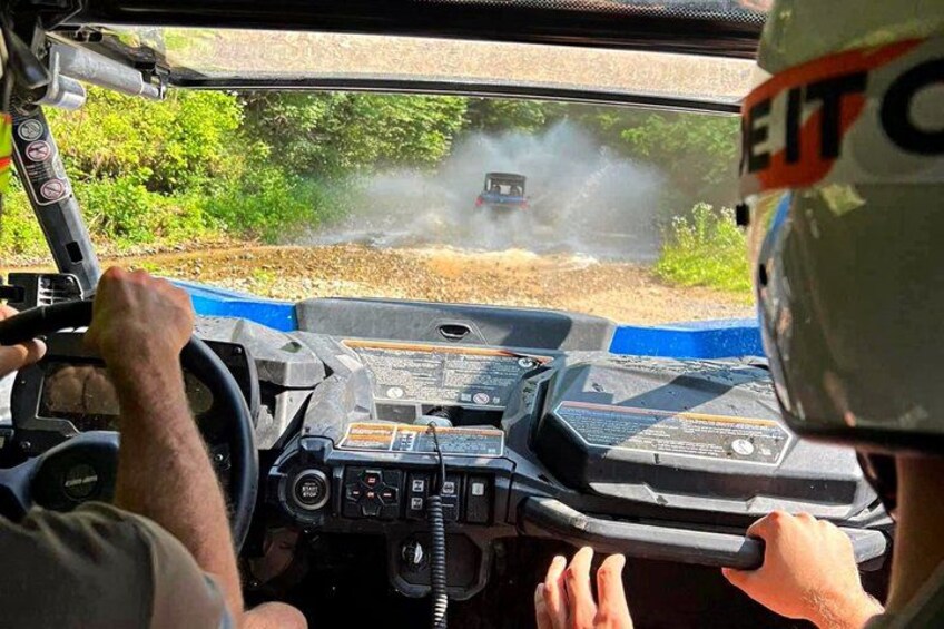A vehicle's dashboard with a steering wheel, a control panel, and a window view of a vehicle on a dirt track. 5