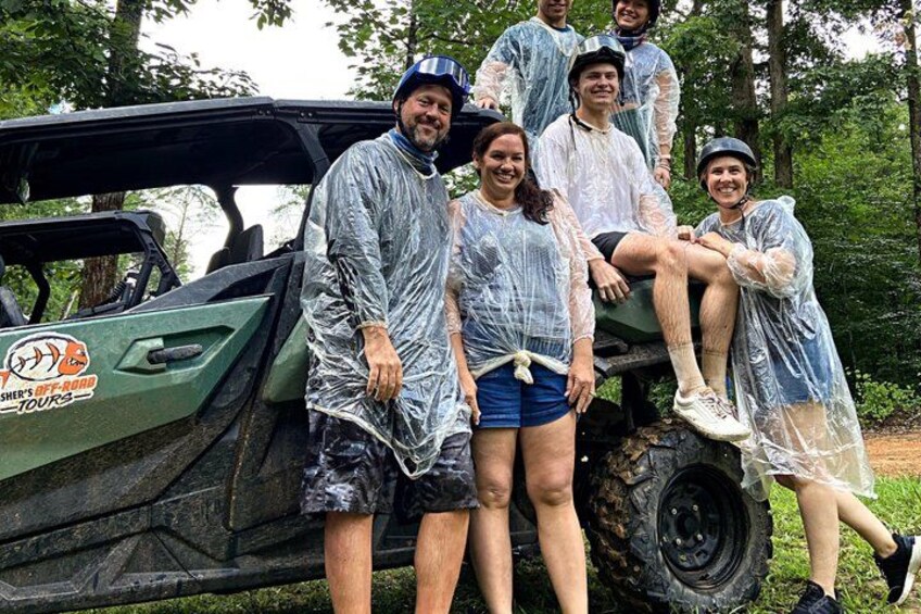 A group of people in rain ponchos posing next to a green off-road vehicle with a logo on the side. 4