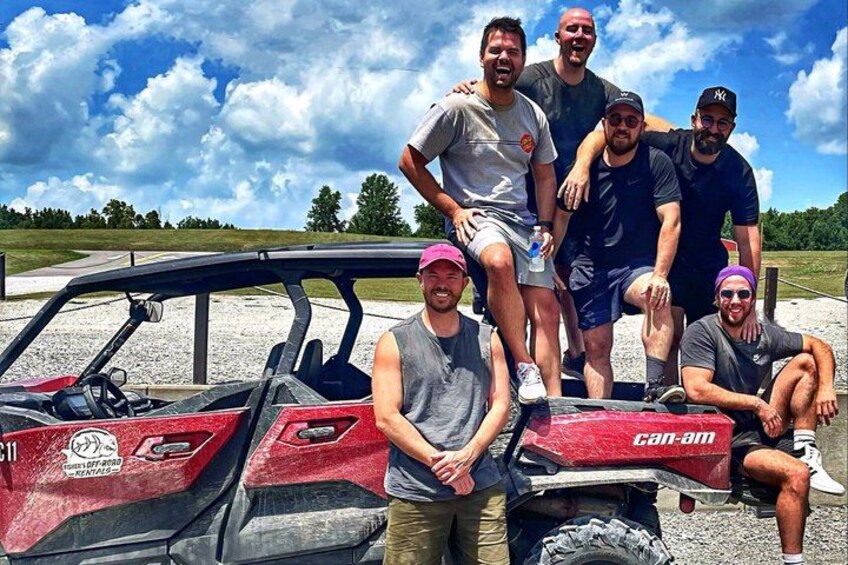 A group of people posing with a red ATV in an open field. 4