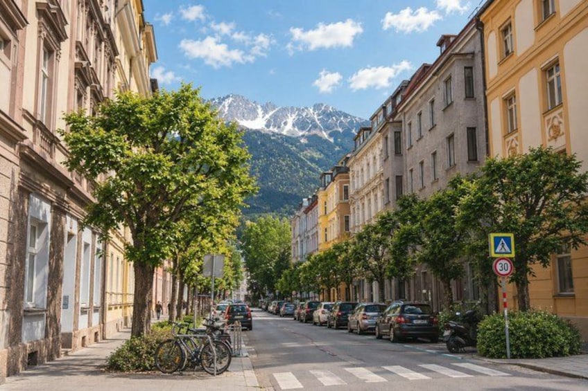A street lined with parked cars and trees, a pedestrian crossing sign, and a mountain in the background. 3