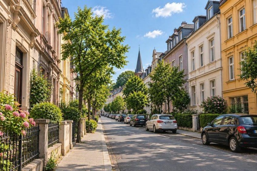 A tree-lined street with parked cars and historic buildings. 4