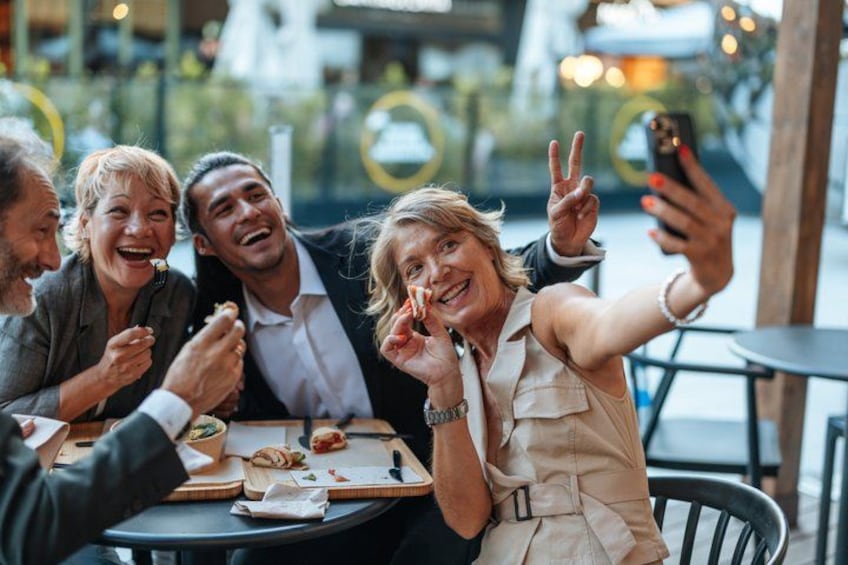 A group of people sitting at a table, eating and taking a selfie. 1