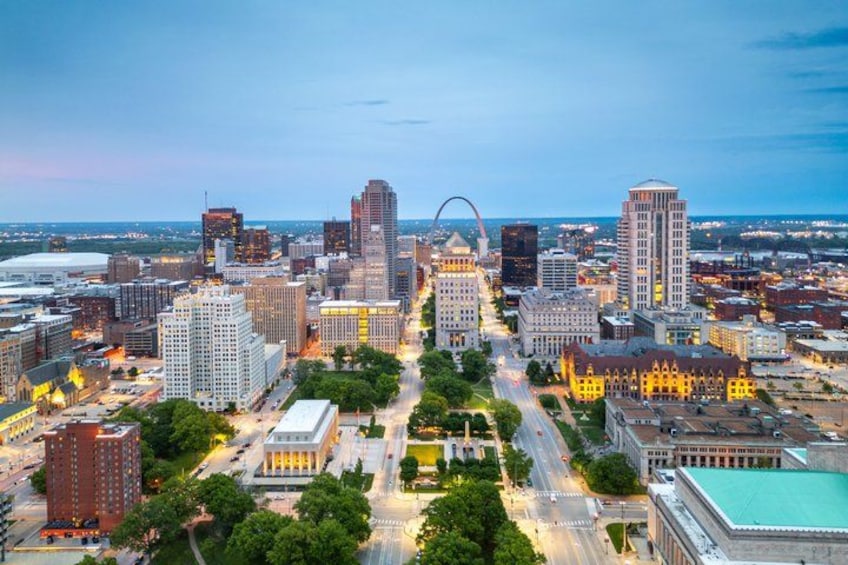 A cityscape with a prominent arch structure, various buildings, and a large body of water in the distance. 3
