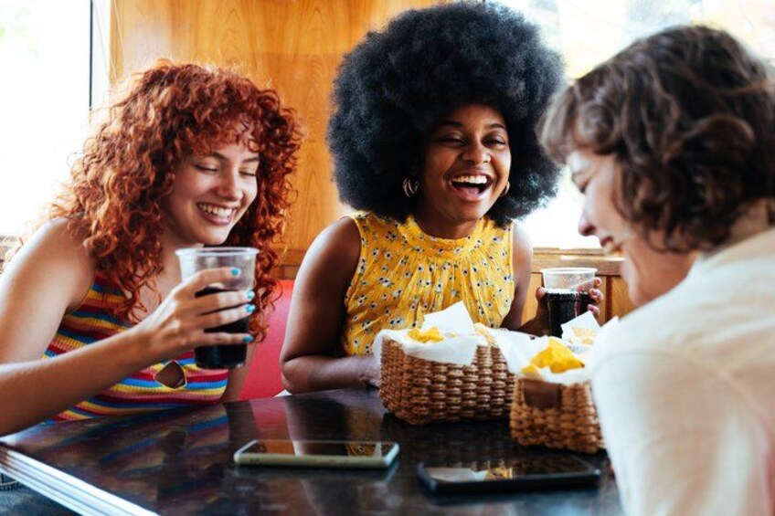 Three people sitting at a table with drinks and snacks. 5