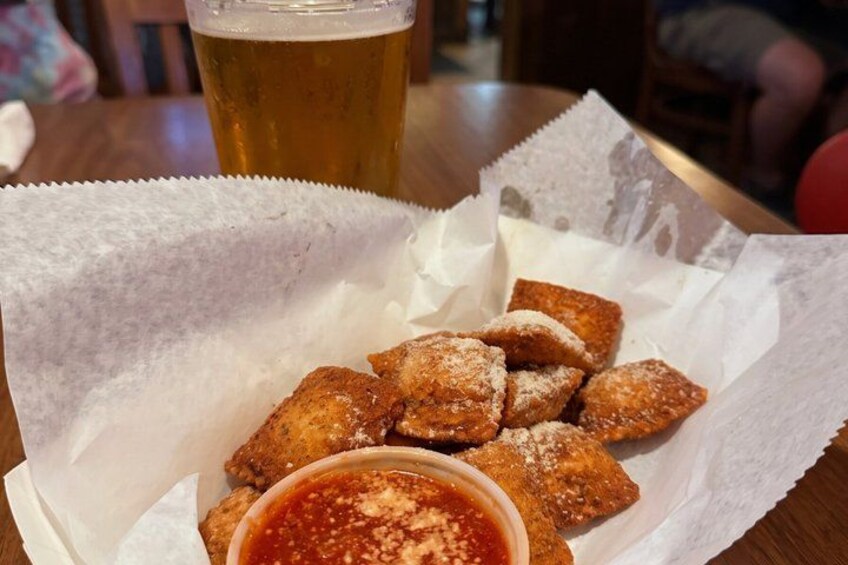 A tray of fried dough sticks with a dipping sauce, a glass of beer, and a paper liner on a wooden table. 4