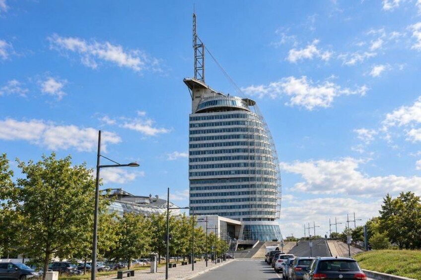 A modern curved skyscraper with a crane on top, surrounded by a tree-lined street and parked cars. 2
