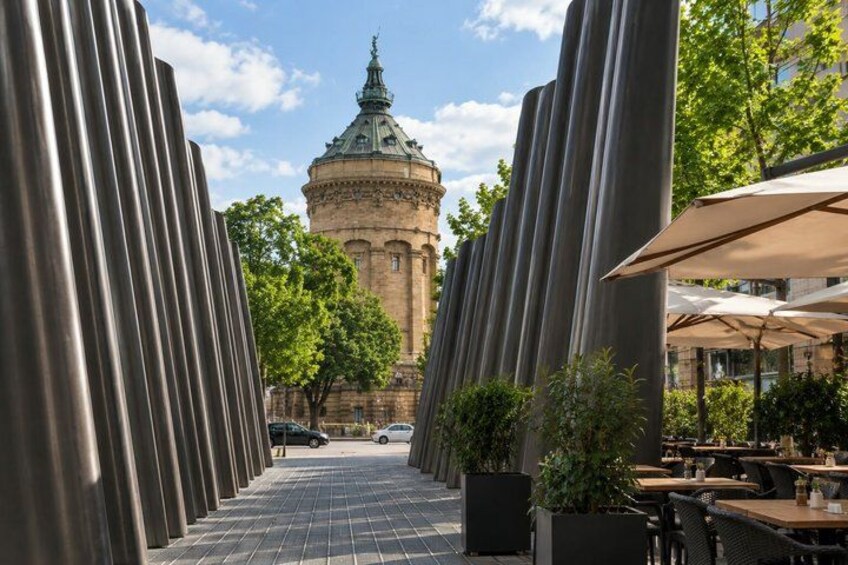 A plaza with a historic tower, metal sculptures, and outdoor seating. 4