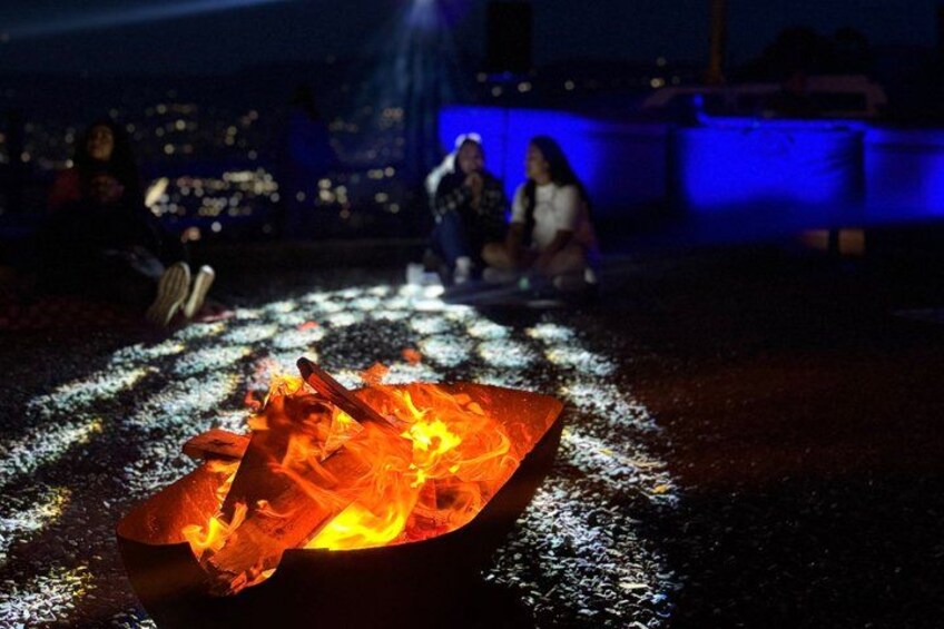 A campfire with flames and a person sitting nearby. 2