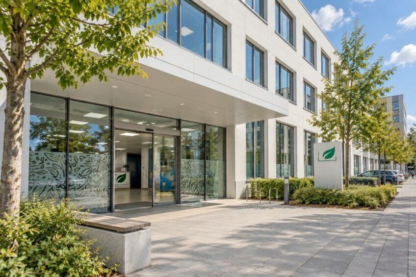 A modern building with large windows, a covered entrance, and a green logo. 5