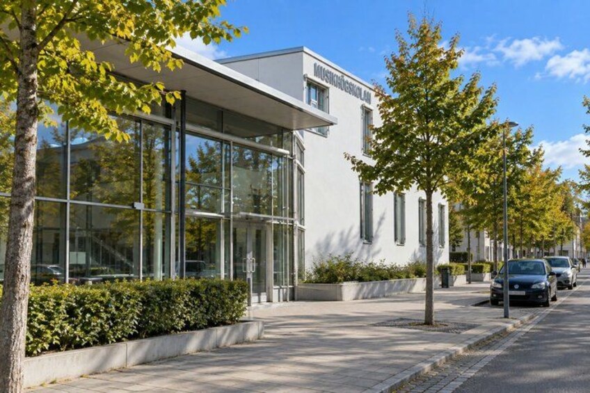 A modern building with large windows, a tree-lined sidewalk, and parked cars. 2