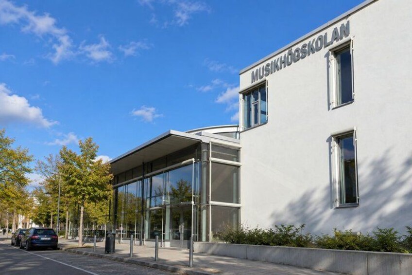 A modern building with a glass facade and the name 'MUSIKHÖGSKOLAN' on the side. 3
