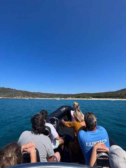 A group of people on a boat with a clear view of a coastline and hills in the background. 2