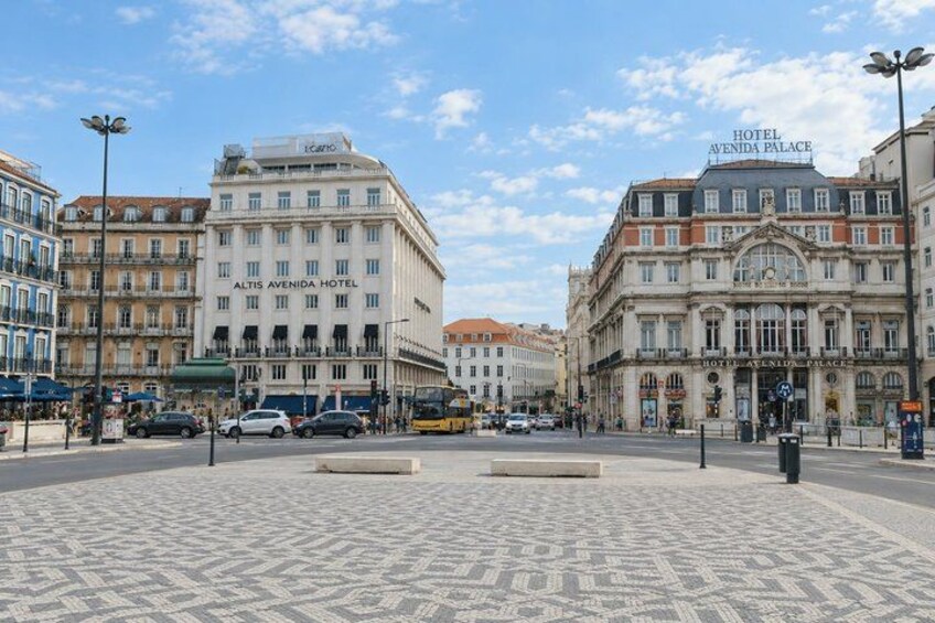 A city square with a patterned pavement, surrounded by historic buildings including the Altis Avenida Hotel and Hotel Avenida Palace. 3
