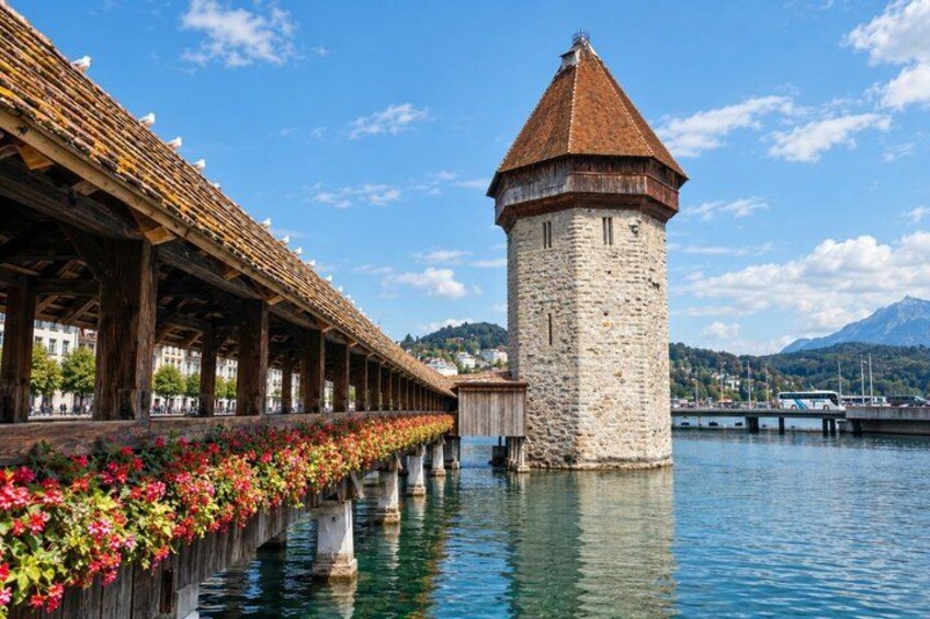 A stone tower, a covered walkway with flowers, and a calm body of water with mountains in the background. 2
