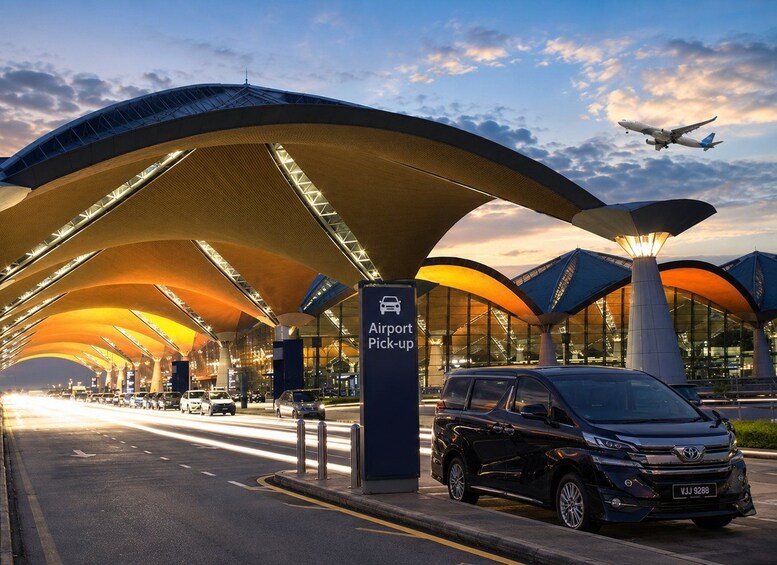 An airport pick-up area with a modern canopy structure and a black car parked under it. 4