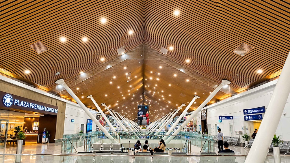 A spacious airport terminal with a wooden ceiling design, a lounge area, and directional signs. 5
