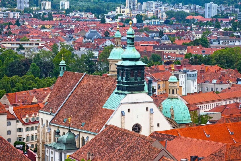A cityscape with red-tiled roofs, historic buildings, and green domes. 2