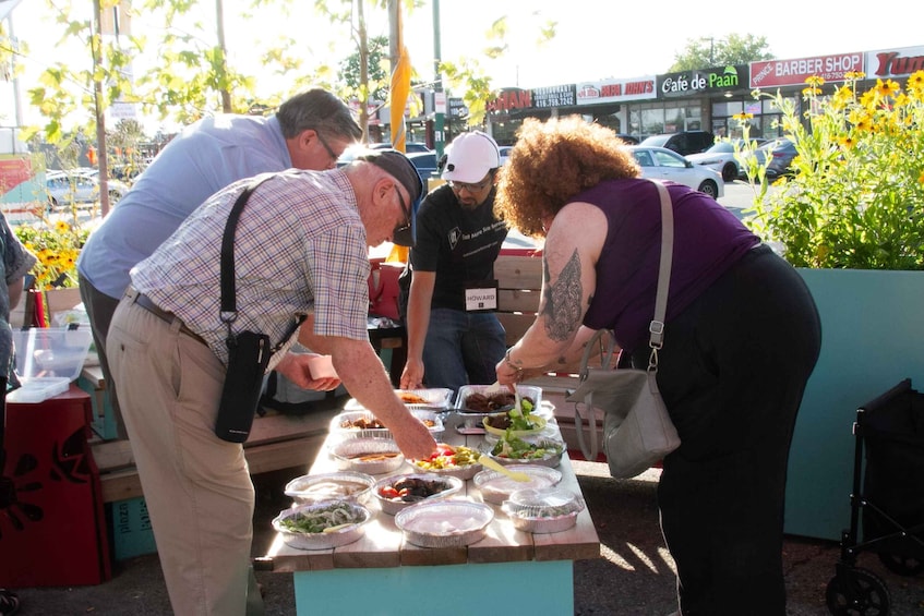 Personas sirviendo comida en un evento al aire libre, con diversos platos sobre una mesa. 2