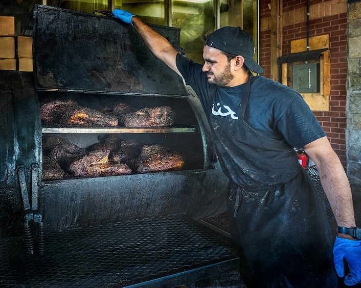 Una persona con camisa y guantes negros manipulando un horno grande con comida en su interior. 3