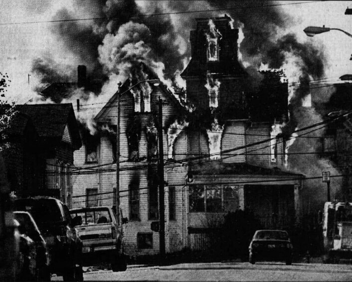 A burning building with thick smoke rising into the sky. 1