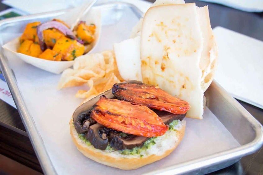 A sandwich with grilled tomatoes and mushrooms on a bun, accompanied by a side of pickled vegetables and a piece of flatbread. 4