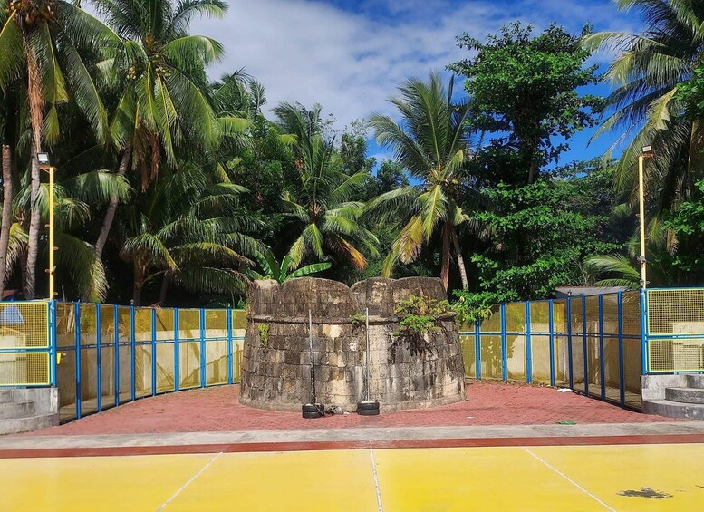 A stone structure surrounded by a blue fence, with palm trees in the background. 2