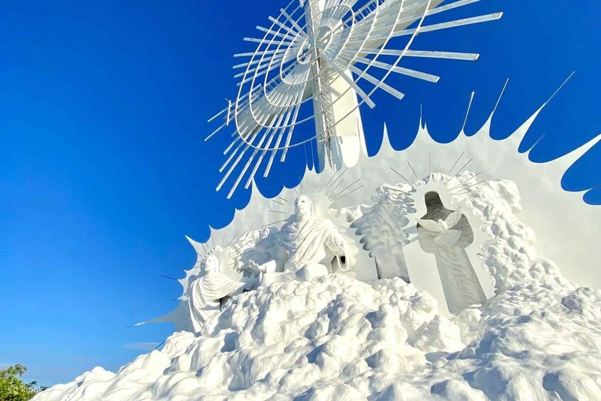 A white sculpture of a figure with outstretched arms, a large white structure resembling a windmill, and a clear blue sky. 1